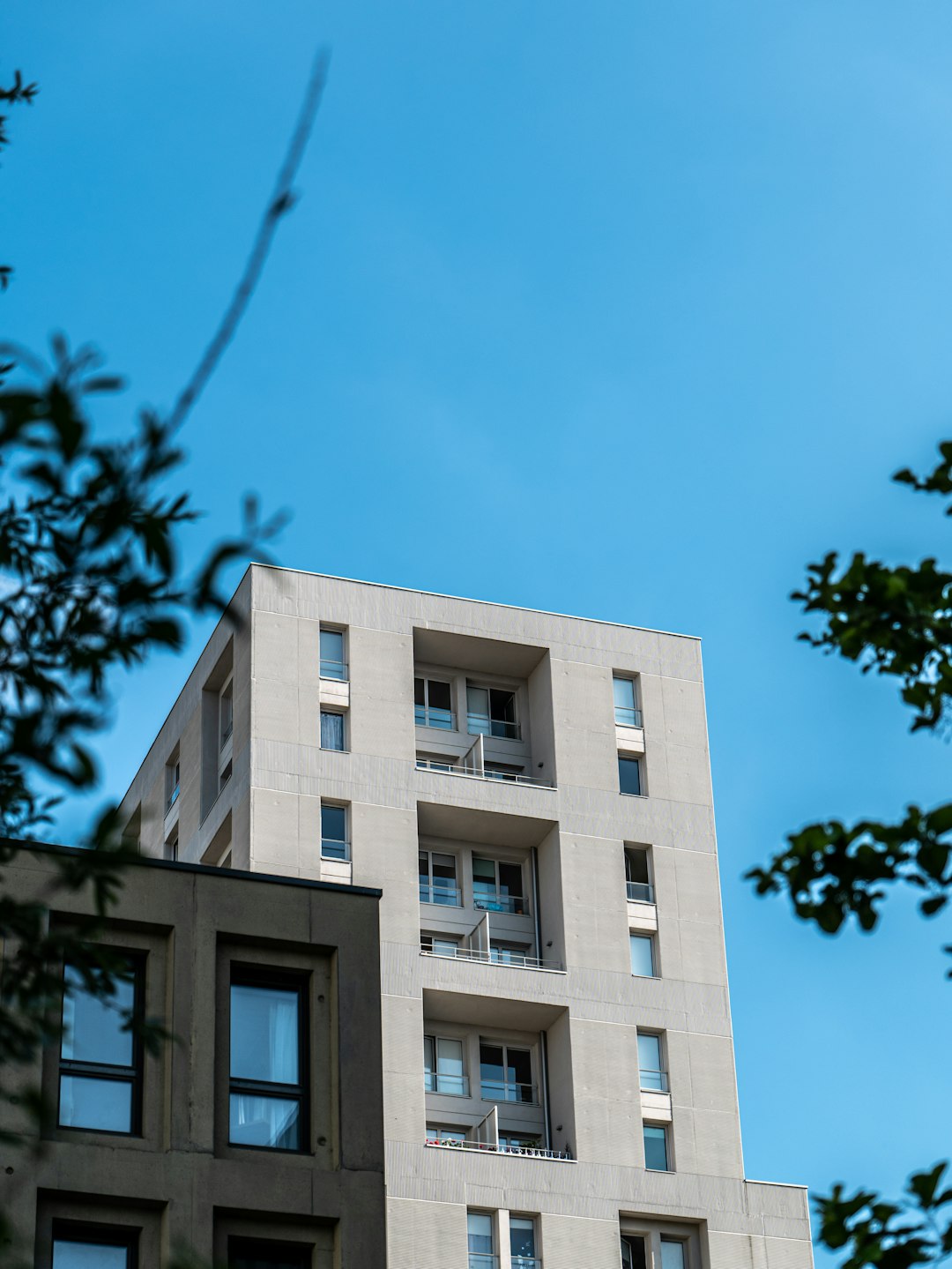 services-02 A modern building in the city of Nantes, captured in a low-angle shot. Reflections of the sky and clouds on the building can be seen. Blue and cloudy sky in the background. Sunny.